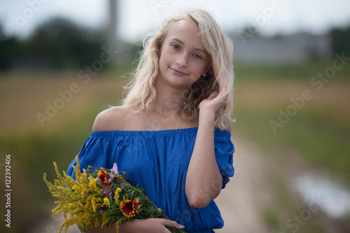 The girl in the blue dress in a field with  bouquet of flowers