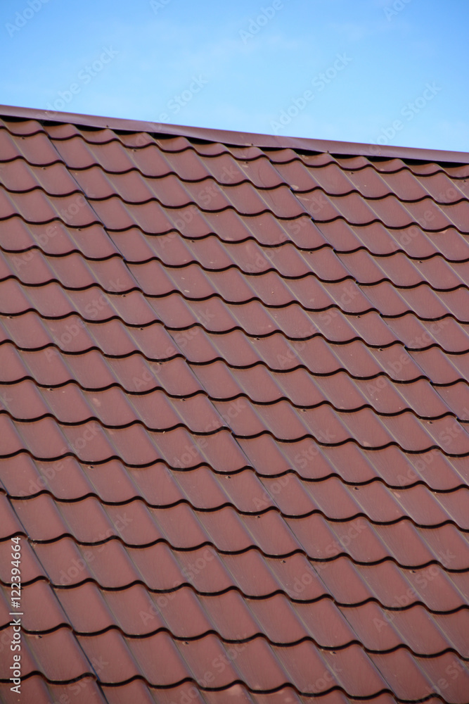 Modern roof covered with tile effect PVC coated brown metal roof sheets against a blue sky