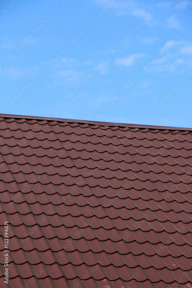Modern roof covered with tile effect PVC coated brown metal roof sheets against a blue sky Modern roof covered with tile effect PVC coated brown metal roof sheets against a blue sky