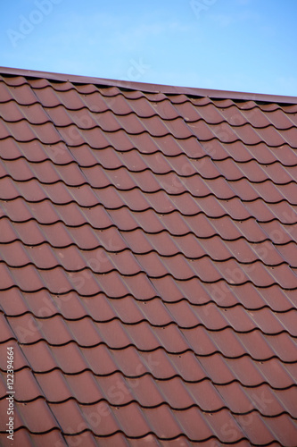 Modern roof covered with tile effect PVC coated brown metal roof sheets against a blue sky