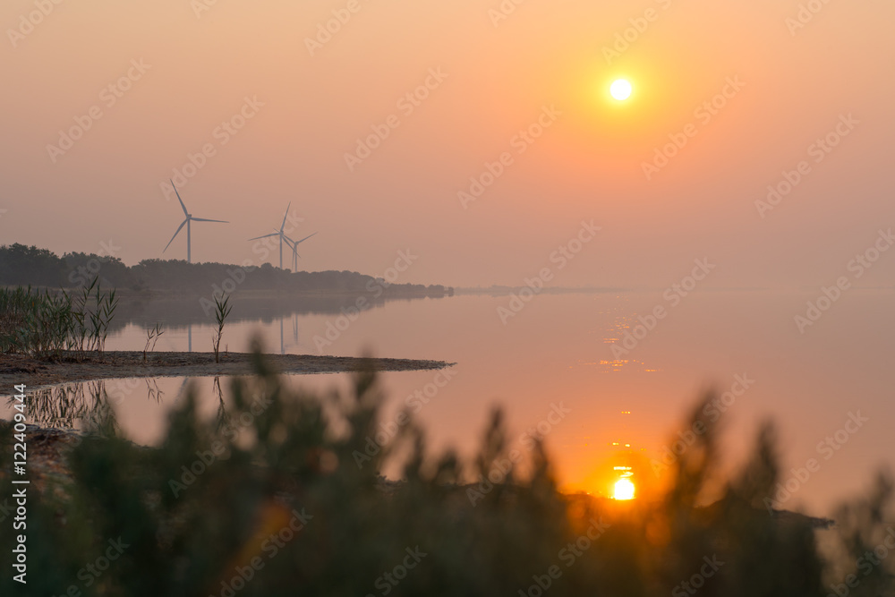 Sunrise over the sea bay. Wind power station on the background Sunrise over the sea bay. Wind power station on the background