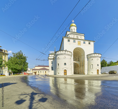 Wide angle view of the Golden Gate in Vladimir, Russia, reflecting in wet asphalt road under blue sky photo