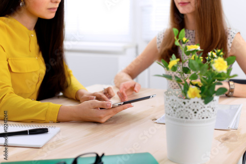 Two business woman or friends are talking and using tablet computer