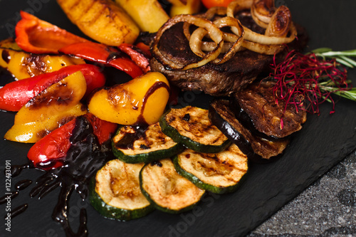 Steak with grilled vegetables and potatoes on stone plate on dark background