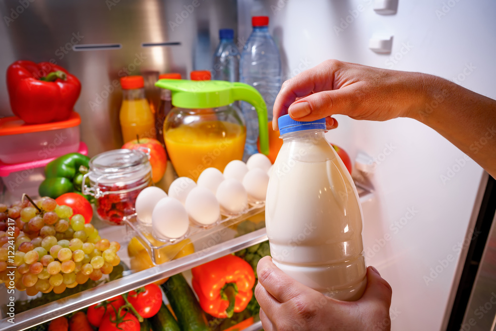 Woman takes the milk from the open refrigerator Woman takes the milk from the open refrigerator