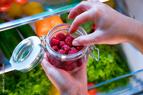 Woman takes the fresh raspberries from the open refrigerator
