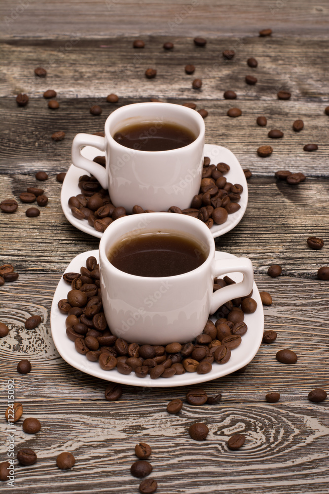 two small white cups of coffee with cocoa beans on wooden background two small white cups of coffee with cocoa beans on wooden background