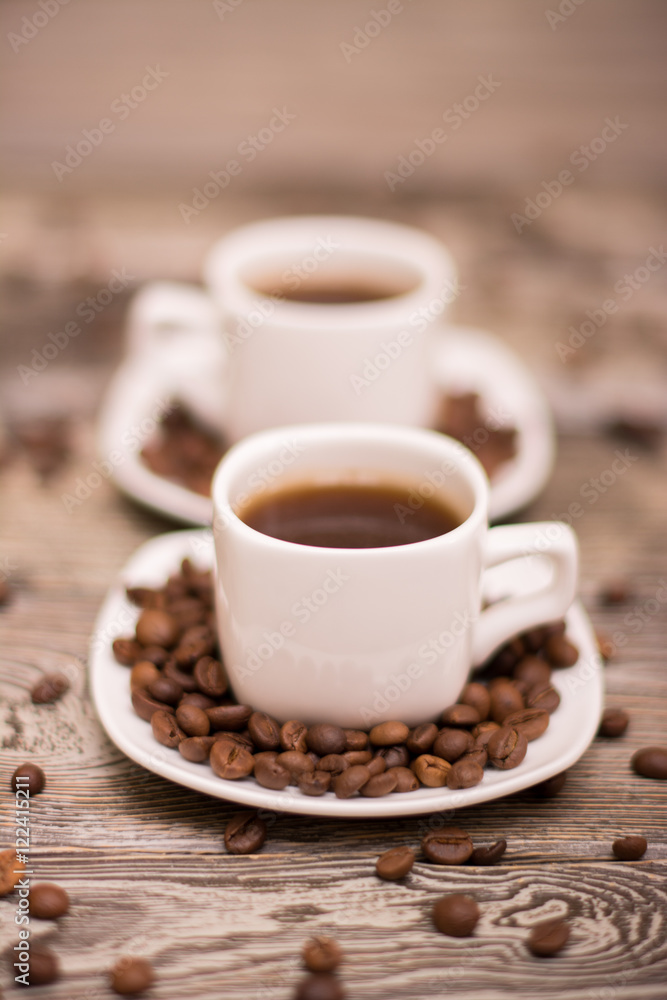 two small white cups of coffee with cocoa beans on wooden background two small white cups of coffee with cocoa beans on wooden background