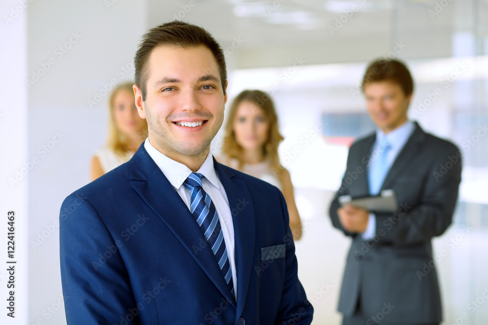 Smiling businessman in office with colleagues in the background Smiling businessman in office with colleagues in the background