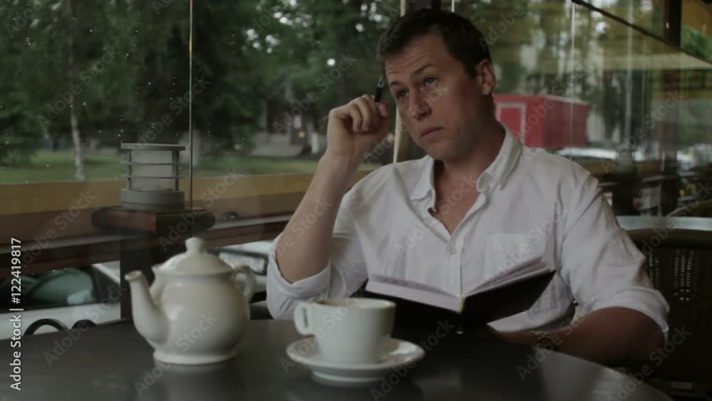 A writer writes poetry and write them in notebook sitting in a summer cafe. A writer writes poetry and write them in notebook sitting in a summer cafe.