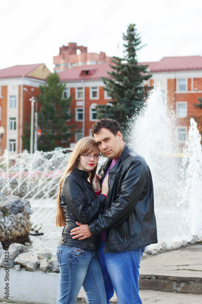 Man embraces woman in black leather jackets near fountain in aut Man embraces woman in black leather jackets near fountain in aut