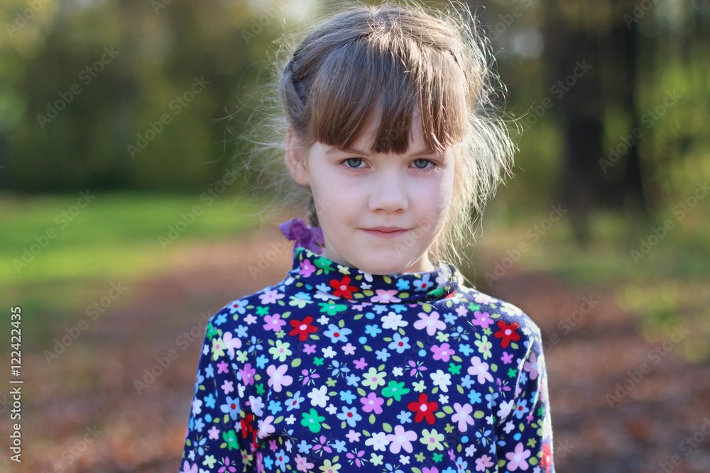 Cute little girl stands in sunny green park, shallow dof, close