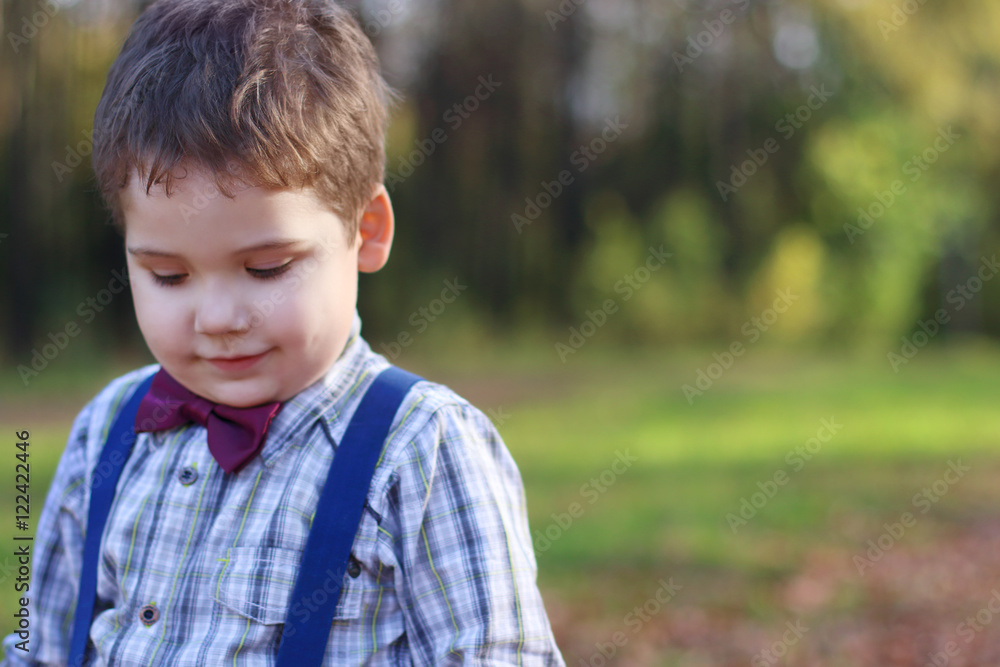 Handsome little boy with bow tie looks down in green park, shall Handsome little boy with bow tie looks down in green park, shall