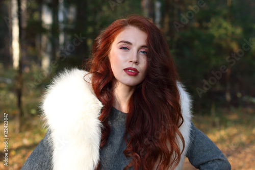 Pretty girl with make up and white fur stands in forest at sunny