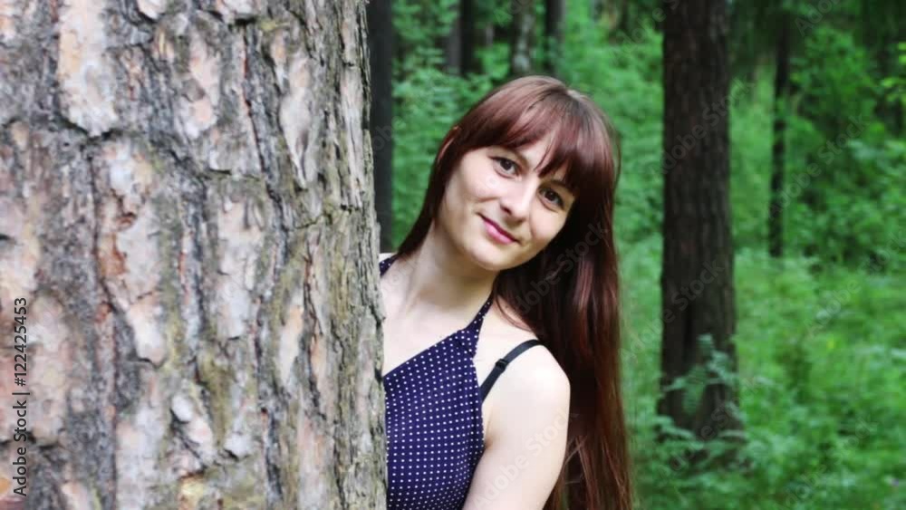 Pretty woman peeking out from behind tree in green summer forest Pretty woman peeking out from behind tree in green summer forest