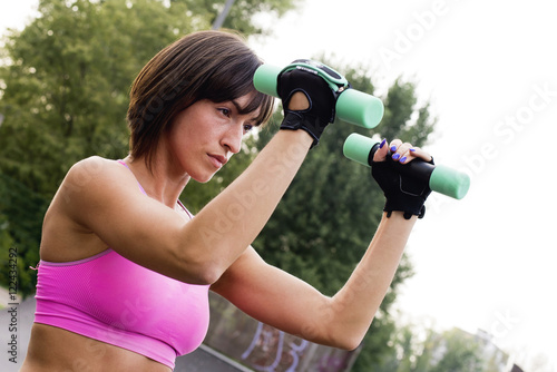 Young girl doing workout with dumbbells outside. 