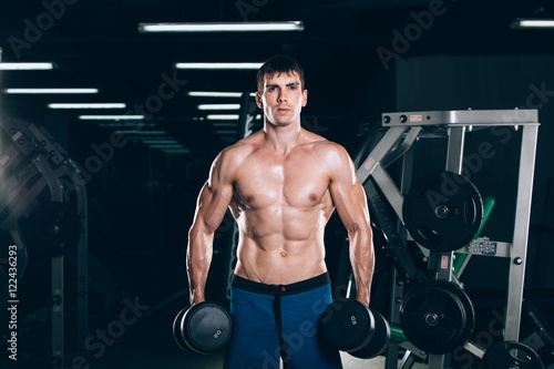 sport, fitness, lifestyle and people concept - Muscular bodybuilder guy doing exercises with dumbbells in gym.