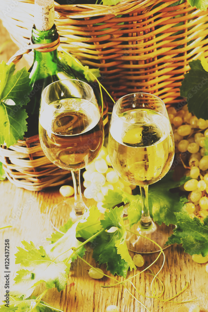 Two glasses and bottle of white wine, grapes with leaves