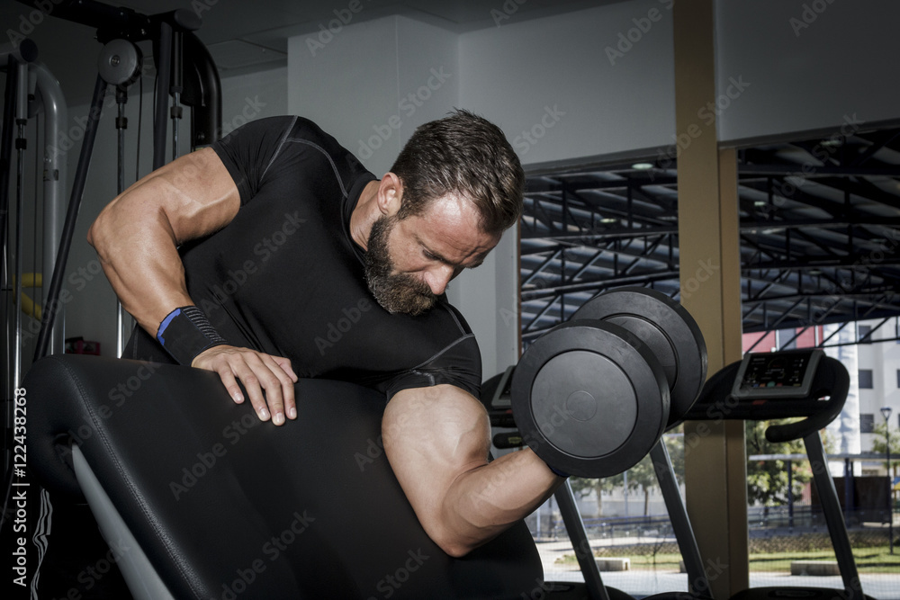 Hombre con grandes músculos levantando peso mientras entrena en el gimnasio. Ponerse en forma.