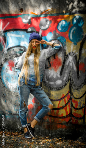 Fashionable girl with long blond hair in stylish clothes standing on a background of graffiti © puhimec