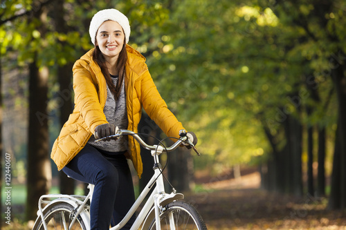 Smiling beautiful woman standing on bike in Autumn park