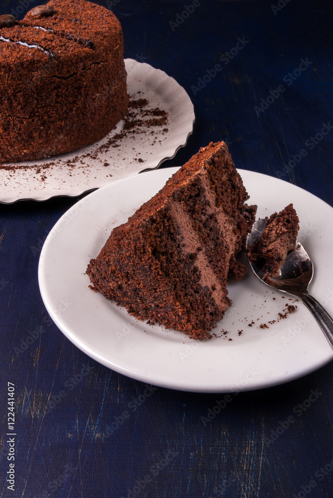 Chocolate cake with cream on a dark blue wooden table, with a spoon, copy space Chocolate cake with cream on a dark blue wooden table, with a spoon, copy space