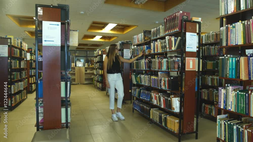 Female student walking in the library at the universit Female student walking in the library at the universit