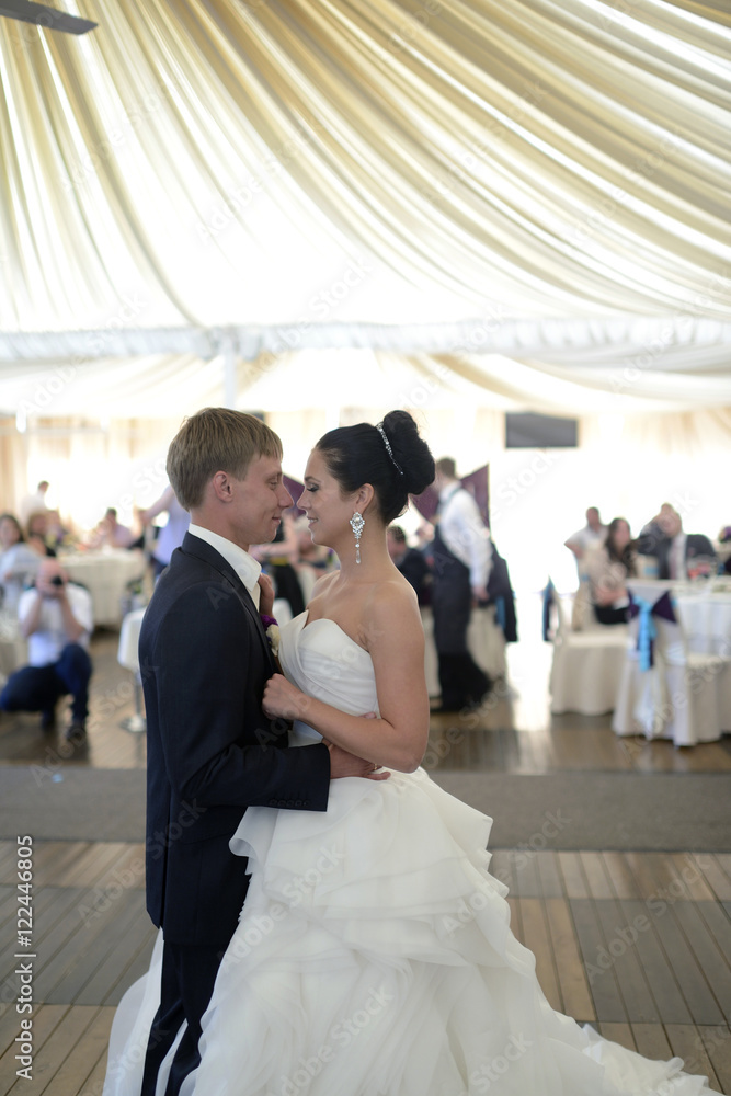 Naklejka premium Wedding couple in the restaurant is dancing. Beautiful model girl in white dress. Handsome man in suit. Beauty bride with groom. Female and male portrait. Woman with lace veil. Lady and guy indoors