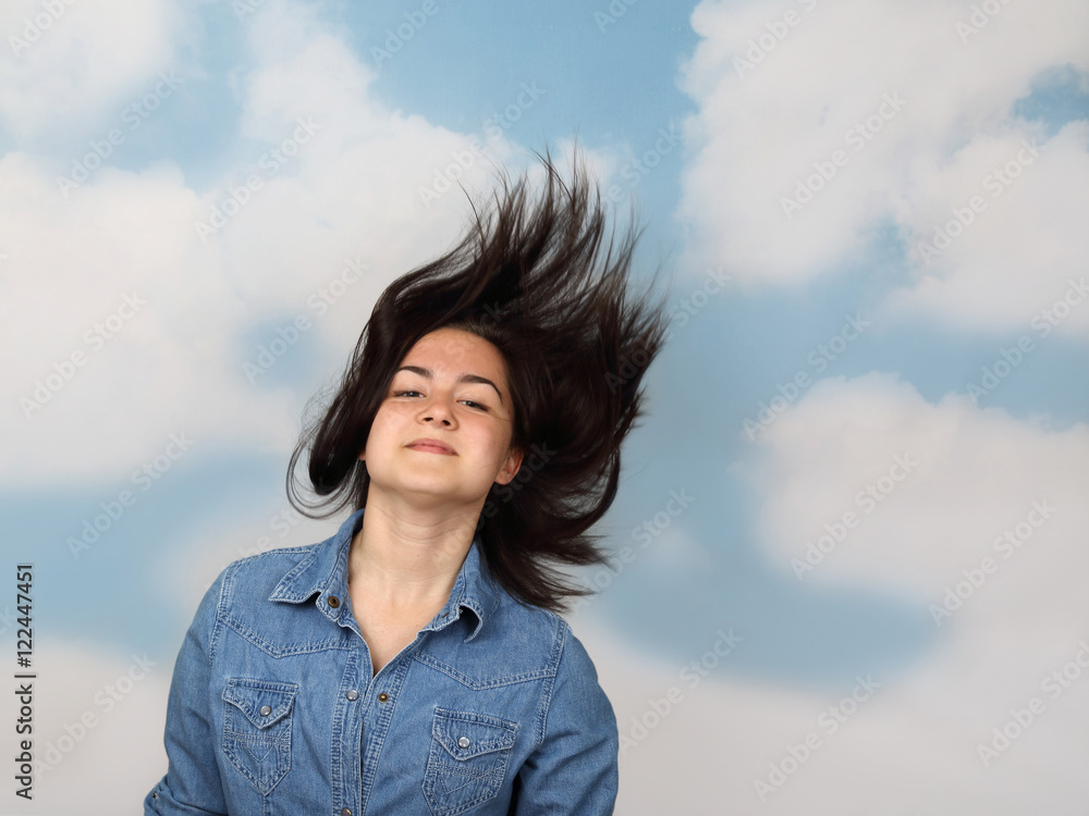 Teenage girl with flowing hair flying in the wind on cloudy blue sky ...