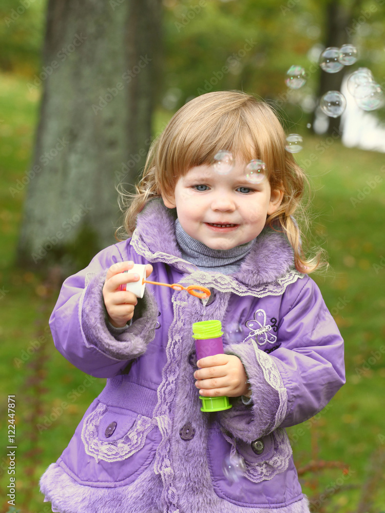 Little girl blows soap bubbles in the park on natural background Little girl blows soap bubbles in the park on natural background