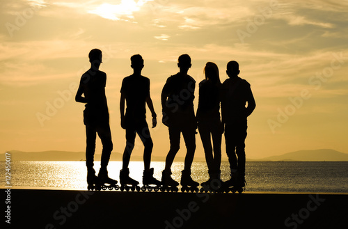 A group of teenage boys and a girl on roller skates at summer, silhouette. 