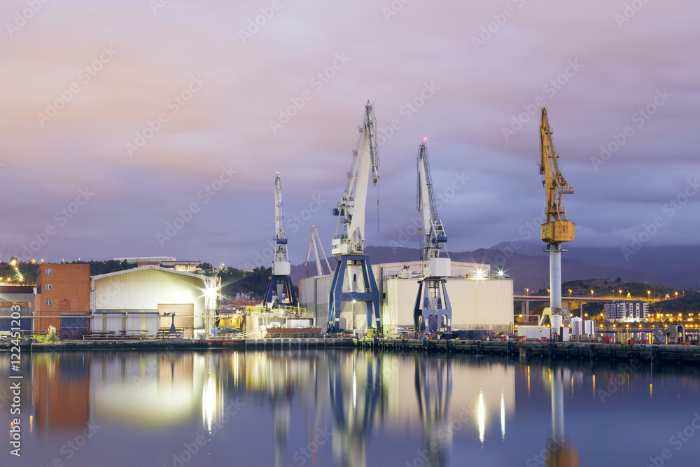 Monumental Cranes at sunrise in Shipyard. Night activity at the naval factories surrounding the city of Bilbao, Spain.