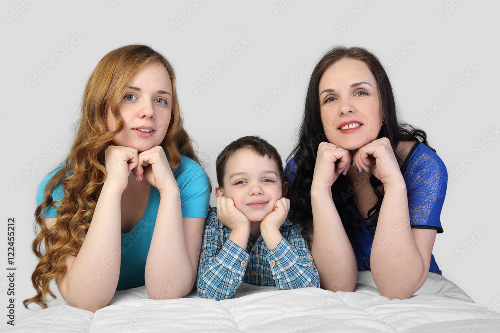 Woman, girl and little boy lie on white blanket looking forward on gray background - incomplete family