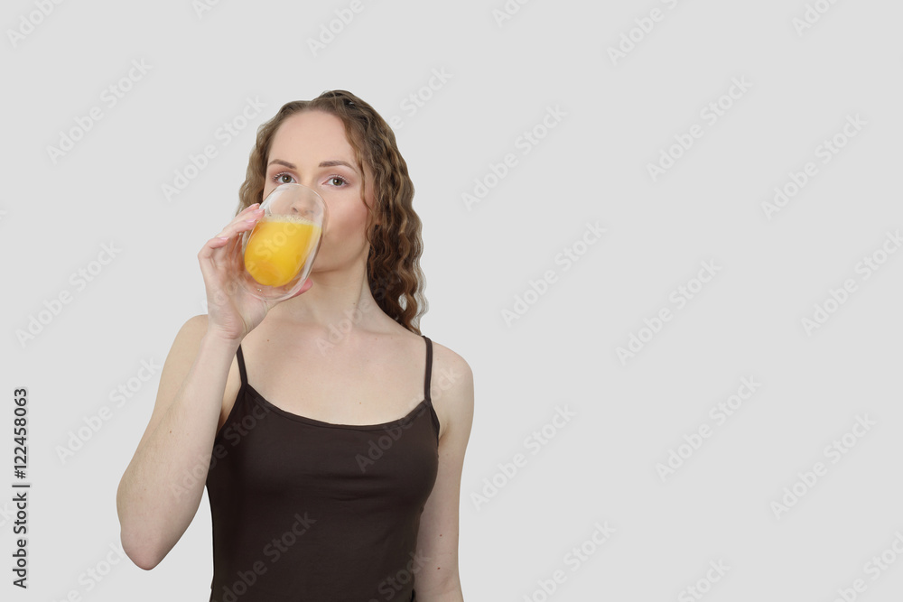 Pretty young woman drinks orange juice on gray background with copy space for text Pretty young woman drinks orange juice on gray background with copy space for text