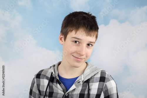 Attractive smiling teenage boy portrait on cloudy blue sky background