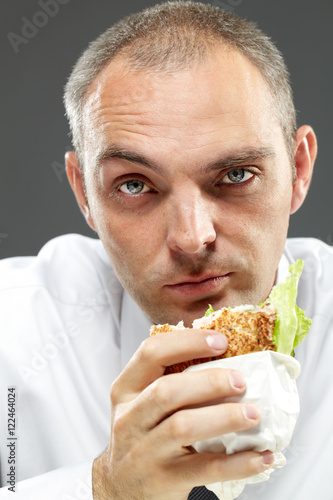 Serious man eating sandwich grey bckground