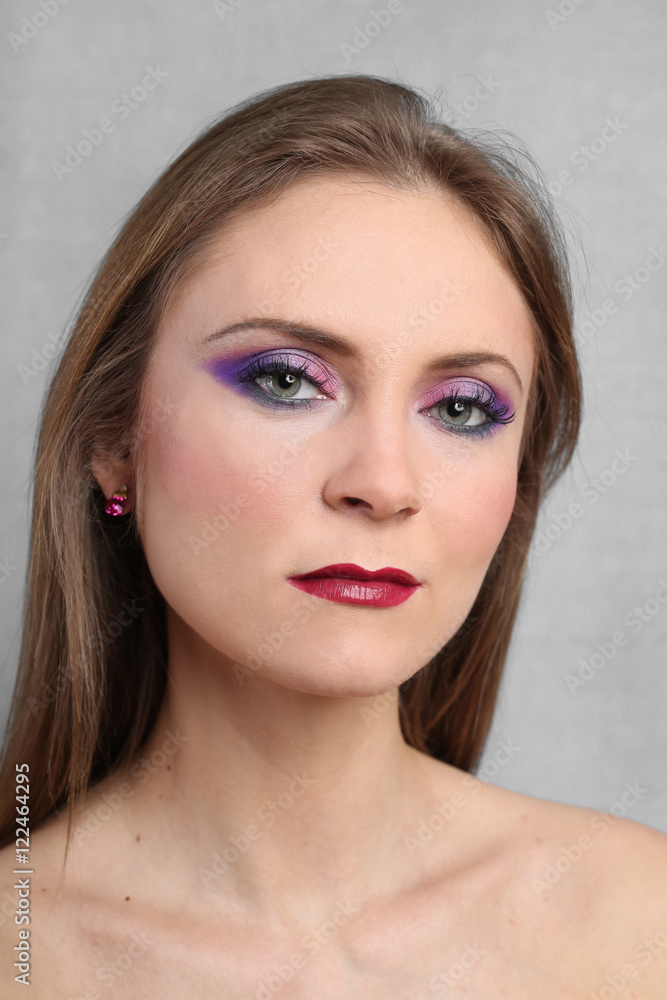 Pretty young woman with bright evening makeup on serious face close up on gray background Pretty young woman with bright evening makeup on serious face close up on gray background