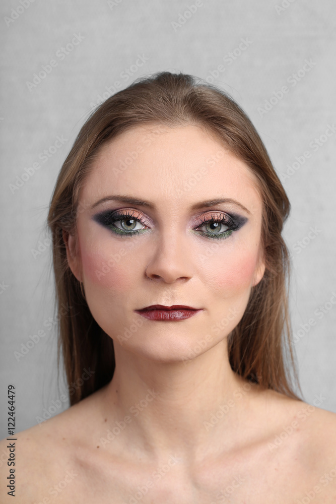 Pretty young woman with bright evening makeup on serious face close up on gray background Pretty young woman with bright evening makeup on serious face close up on gray background
