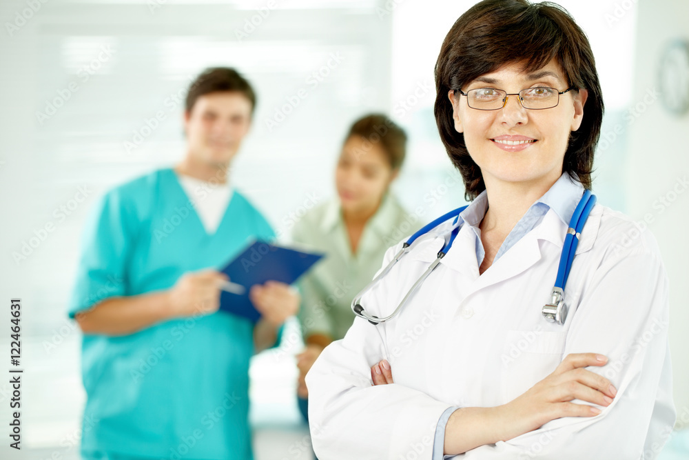 Portrait of beautiful female doctor looking at camera with her colleagues behind Portrait of beautiful female doctor looking at camera with her colleagues behind