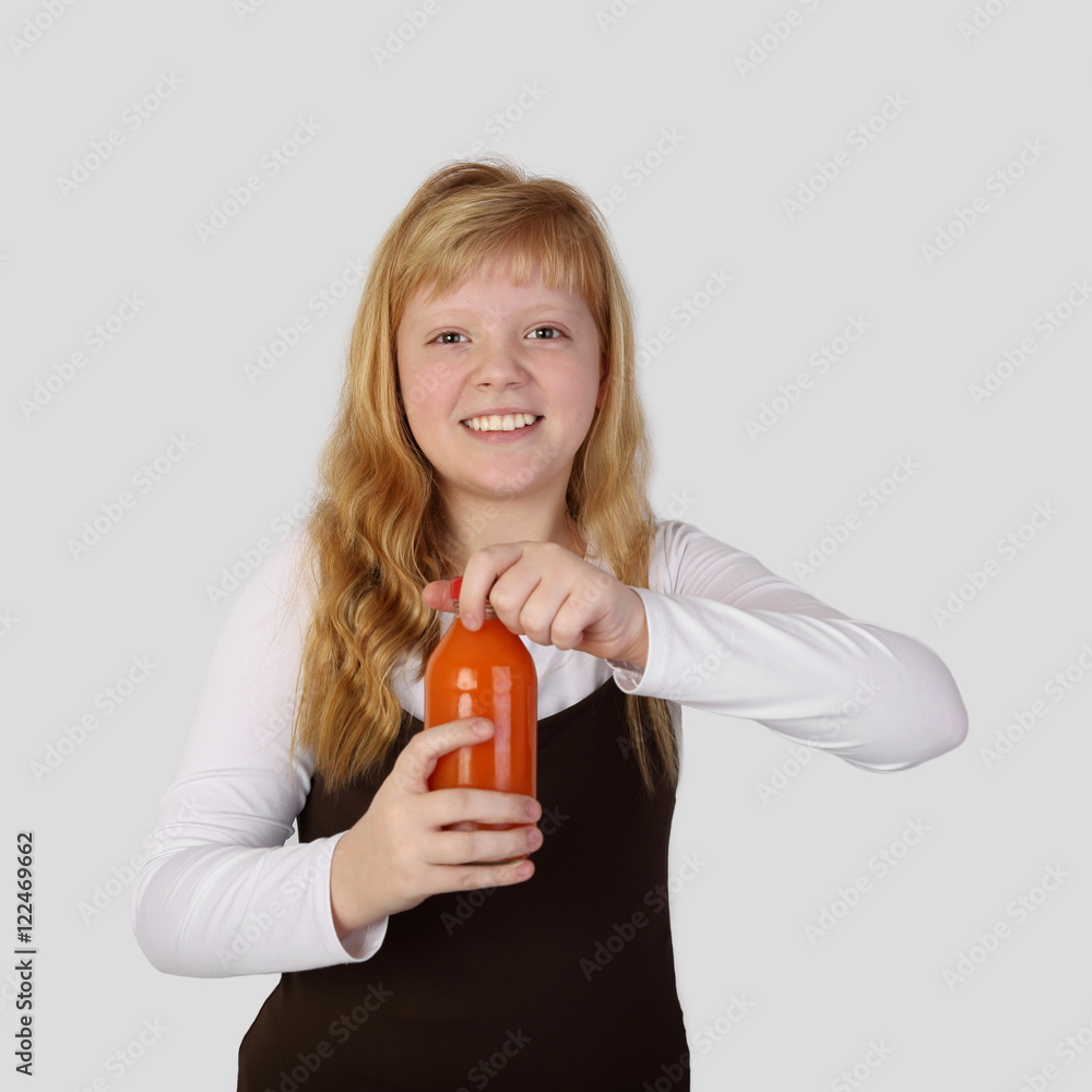 Teenage blonde girl with happy smile opens a bottle of orange carrot juice on gray background in square Teenage blonde girl with happy smile opens a bottle of orange carrot juice on gray background in square
