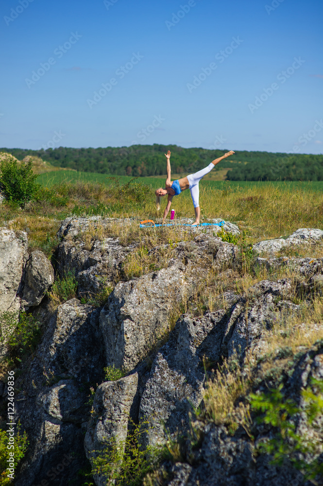 Young beautiful blonde woman doing yoga exercises on a rock. Han