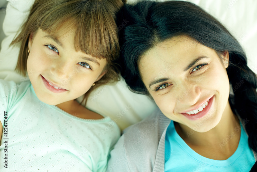 Smiling mother and her daughter lying in bed and looking at camera Smiling mother and her daughter lying in bed and looking at camera