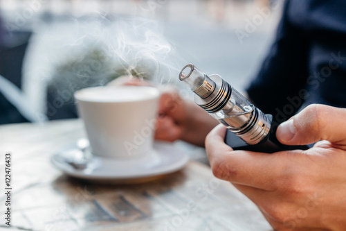 man using vape or electronic cigarette and drinking coffee