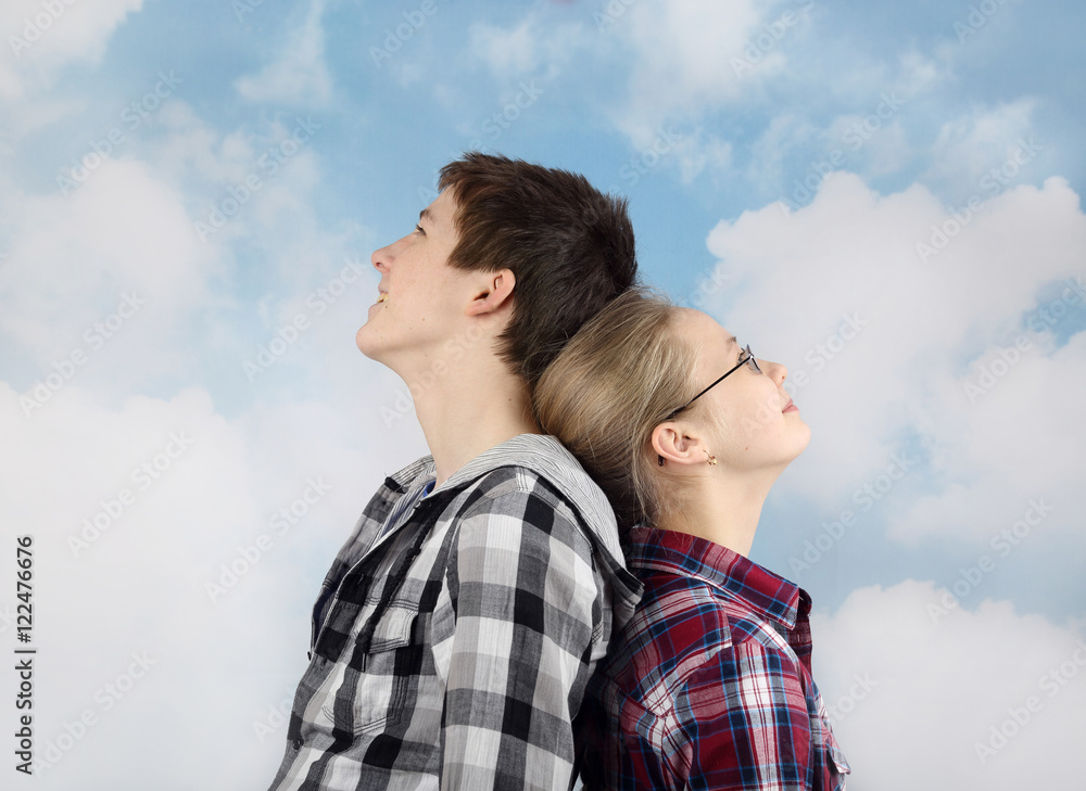 Teenage relationship and friendship - Boy and girl in plaid shirts stand back to back and looking thoughtfully into the cloudy blue sky Teenage relationship and friendship - Boy and girl in plaid shirts stand back to back and looking thoughtfully into the cloudy blue sky