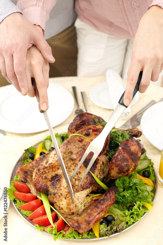 Close-up of roasted turkey on dish with vegetables being cut by a man 