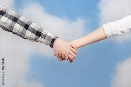 Boy and girl hand in hand on cloudy blue sky background - romantic friendship and togetherness concept