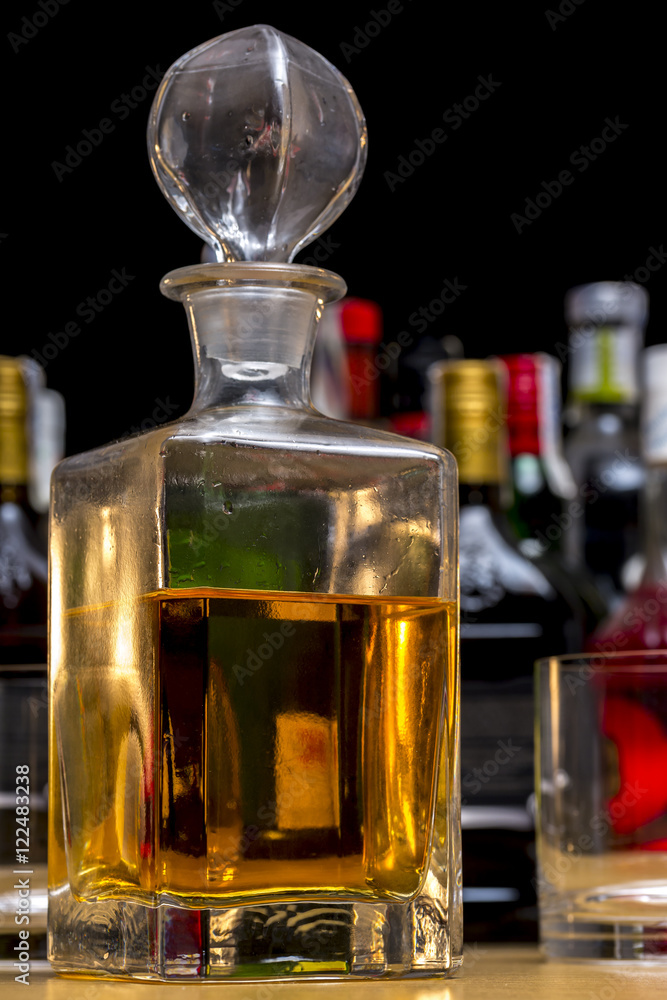 Square glass bottle of malt whiskey in front of several bottles of different alcoholic drinks Square glass bottle of malt whiskey in front of several bottles of different alcoholic drinks
