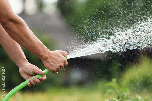 Man watering the garden from hose on sunny day photo