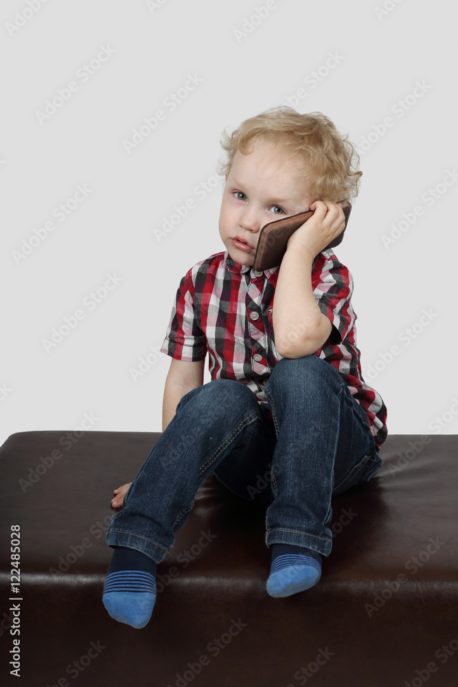 Little boy speaks by cell phone on gray background Little boy speaks by cell phone on gray background