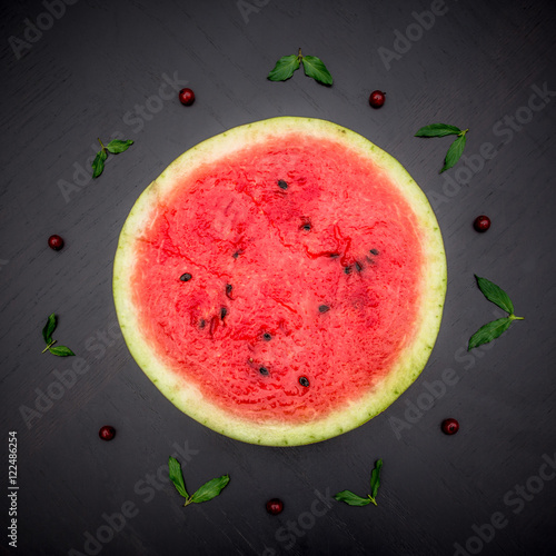 A half of fresh jucie red watermelon on black background. Decorated with mint and wineberry. photo